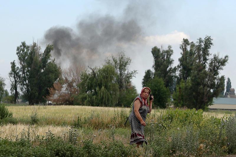 O femeie vorbeste la telefon in regiunea Donetk, in timp ce fumul se ridica in spate, Foto: Anatolii Stepanov / AFP / Profimedia