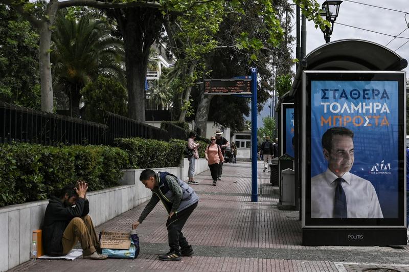 Cerșetor primind bani de la un copil lângă un afiș electoral al premierului grec Kyriakos Mitsotakis, Foto: SPYROS BAKALIS / AFP / Profimedia