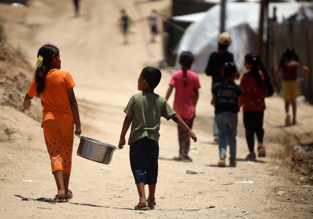 Copii palestinieni strămutați primesc alimente într-o tabără unde locuiesc din cauza bombardamentelor israeliene asupra Fâșiei Gaza, în Deir el-Balah, pe 26 iunie 2024. Foto: Majdi Fathi/NurPhoto/Shutterstoc / Shutterstock Editorial / Profimedia