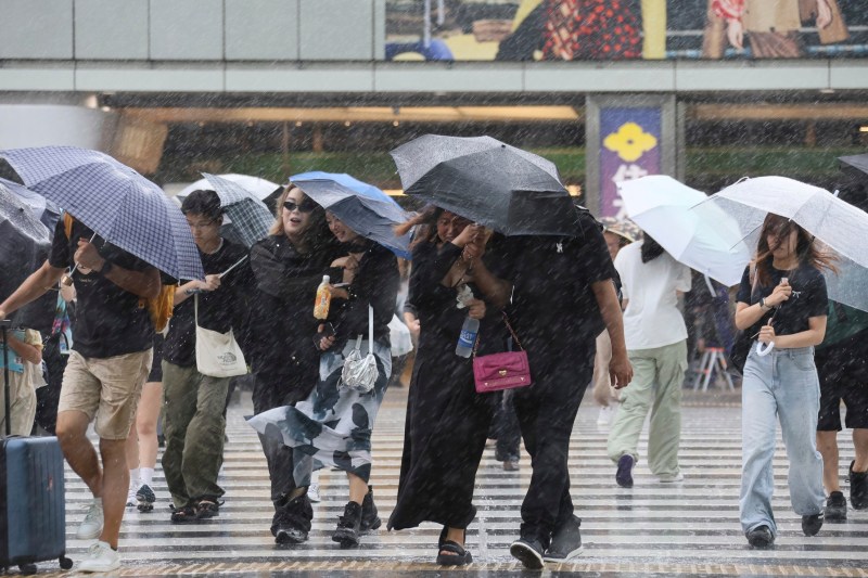 Oamenii se plimbă pe străzile din Shinjuku ,Tokyo, Japonia în ploaie puternică și vânt pe 16 august 2024. Taifunul Ampil se apropie vineri de Tokyo. Foto: Kaname Yoneyama / AP / Profimedia