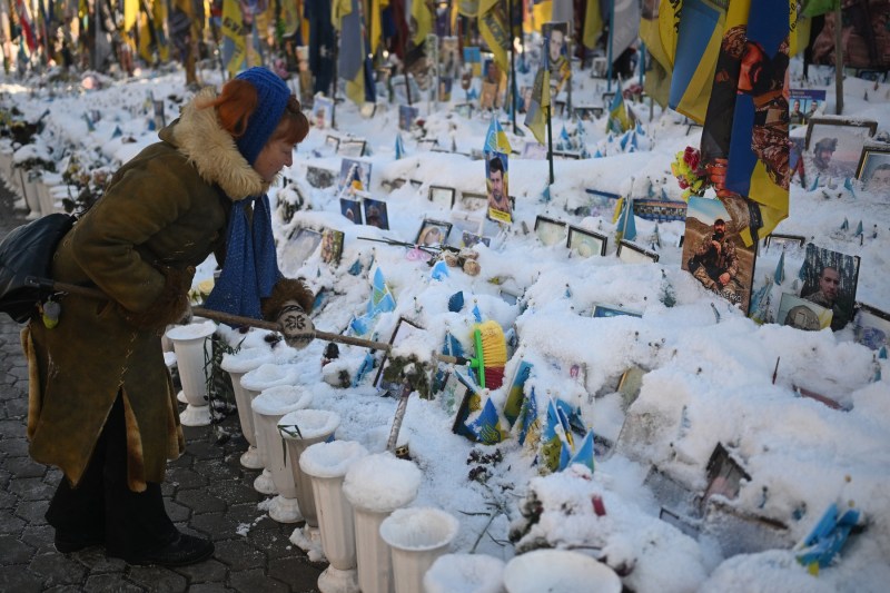 O femeie din Kiev curăță zăpada de pe portretele celor căzuți în războiul cu Rusia, la memorialul din Piața Independenței, 21 ianuarie 2026. Foto: Sergei GAPON / AFP / Profimedia