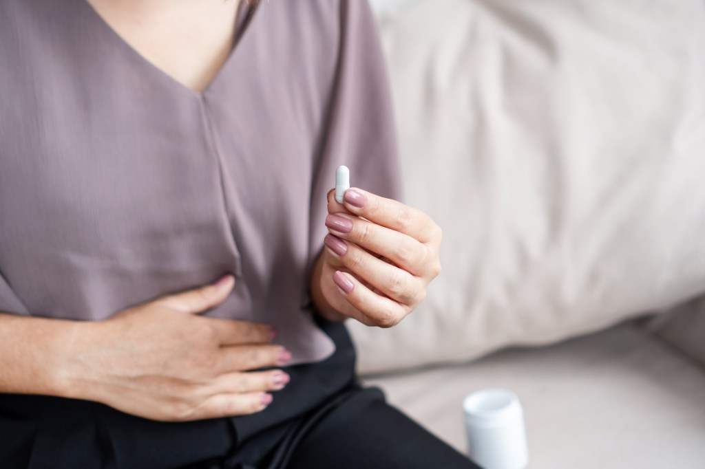 femeie cu durere de burtă care ia un supliment cu probiotice