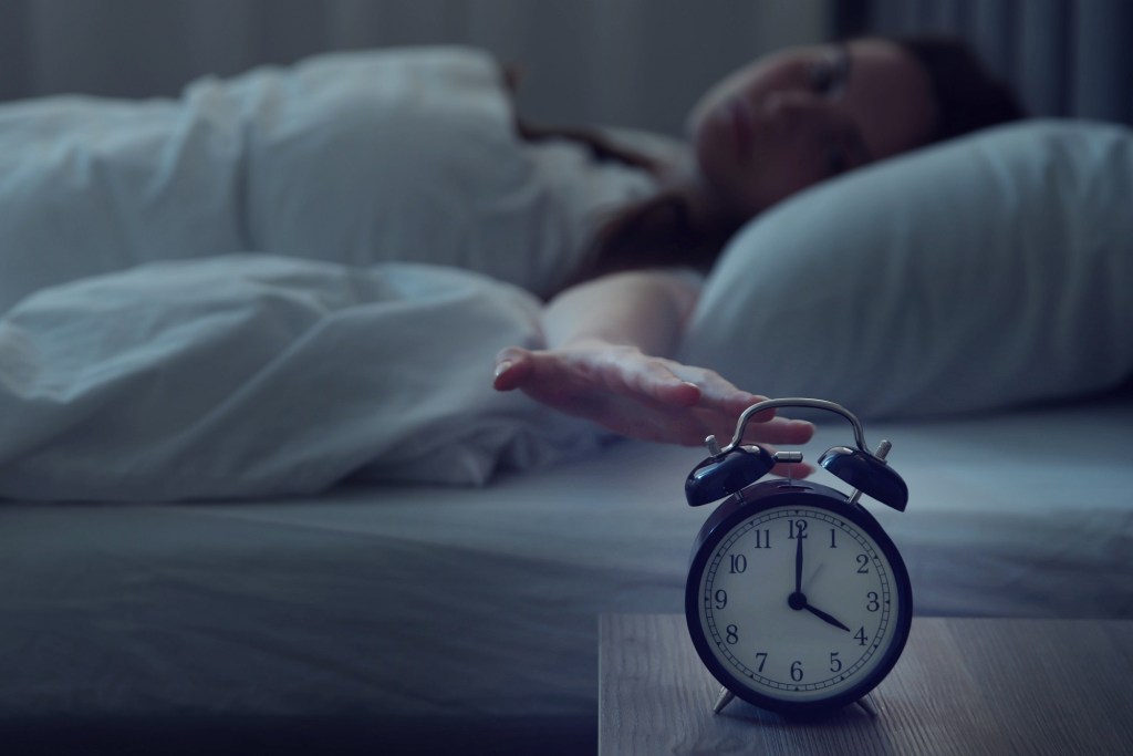 femeie cu insomnie și ceasul deșteptător care indică ora 4