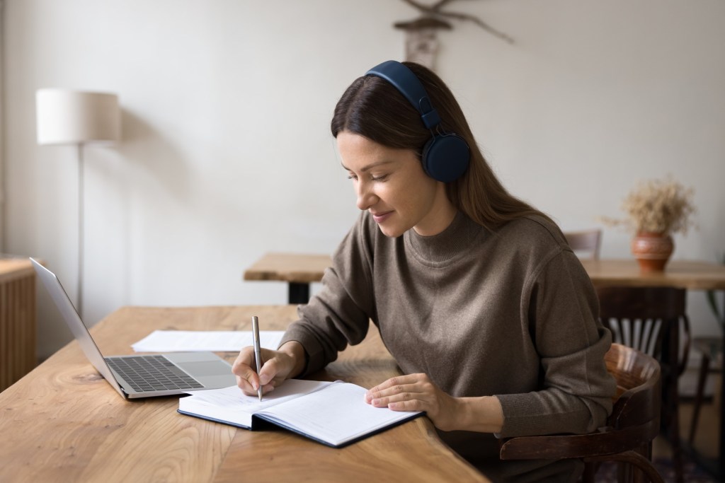femeie învață limbă străină cu laptopul, dar își ia și notițe în agendă