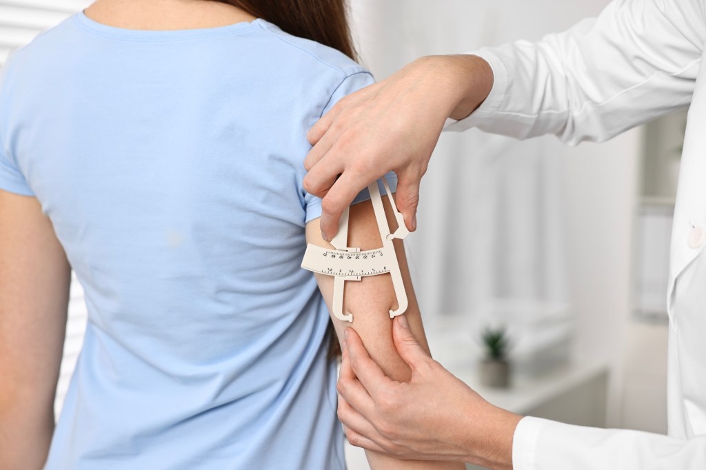 femeie căreia medicul îi măsoară nivelul de grăsime de pe brațe