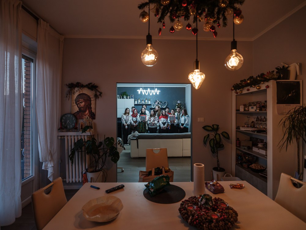 Un grup de tineri colindă la casa unei familii de români din Forlì. Au între 20 și 30 de ani și s-au născut sau au crescut în Italia, unde se află una dintre cele mai mari și mai vechi comunități de români din diaspora. Identitatea lor este modelată în primul rând de școala și societatea italiană, dar își doresc să păstreze și elemente din identitatea lor românească. Așa că, de Crăciun, merg să colinde în română – chiar dacă între ei vorbesc în italiană, care este, în realitate, limba lor nativă. 24 decembrie 2024        Foto: Cosmin Bumbuț, Teleleu 