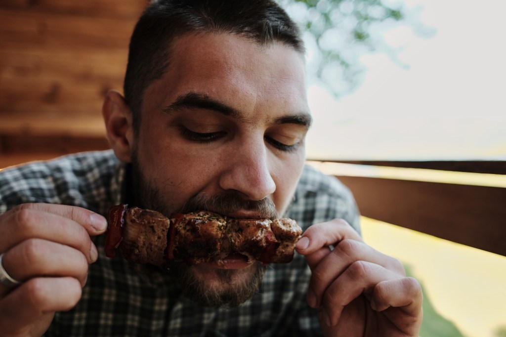 bărbat mușcă dintr-o frigăruie cu carne de pui