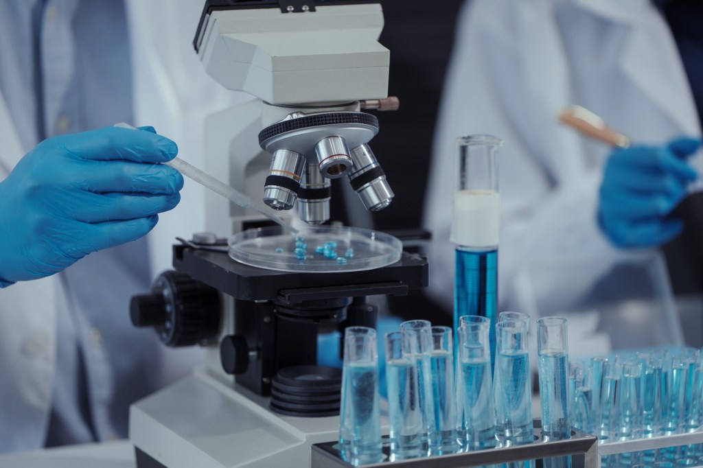 cercetător în laborator cu eprubete și microscop