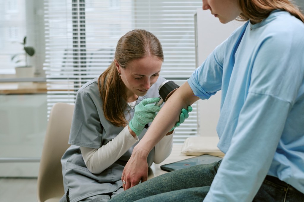 femeie la dermatolog, pielea brațului este examinată cu dermatoscopul