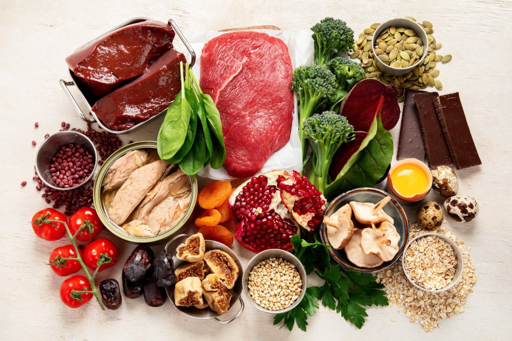 o masă plină cu alimente bogate în fier: carne roșie, ficat, pește, legume verzi, cereale, ciocolată neagră
