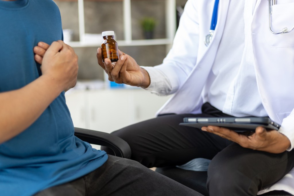 bărbat cu mâna la inimă primește de la medic o sticluță cu pastile