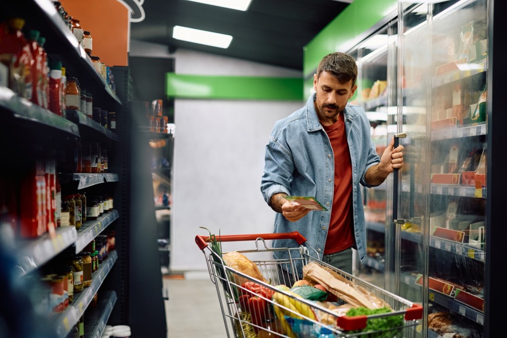 bărbat care citește eticheta alimentelor pe care le pune în coș la supermarket